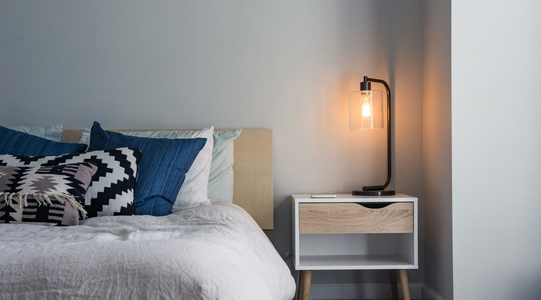 Cama arrumada com um candeeiro de cabeceira aceso, num quarto calmo