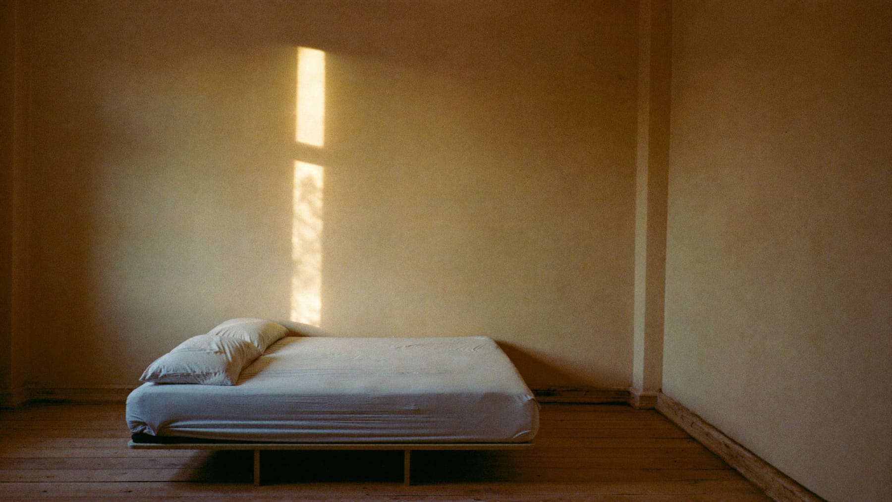 Quarto de manhã cedo, com uma faixa de luz solar a descer pela parede até um colchão no chão